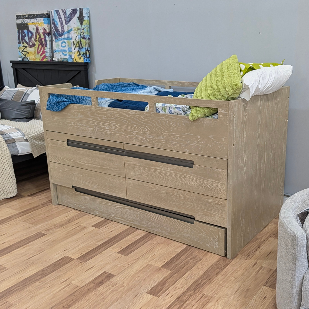 A light oak wood twin-over-one bed frame with integrated drawers and dark metal handles, styled with bedding and pillows in a bedroom setting.